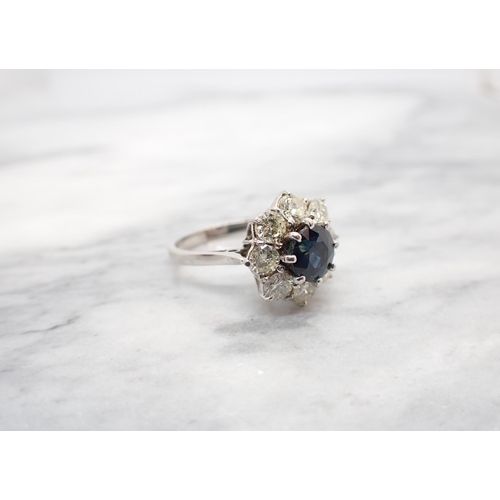 198 - A Sapphire and Diamond Flower Cluster Ring claw-set round sapphire within a frame of eight brilliant... 