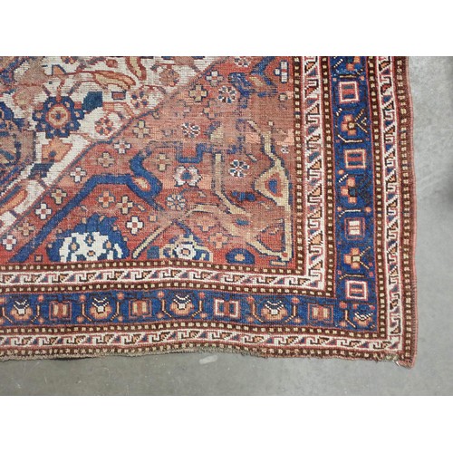 111 - A red ground Persian Rug with stylised floral design on blue medallion 6ft 1in L x 4ft 11in W