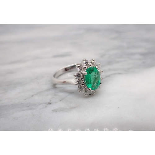 178 - An Emerald and Diamond Cluster Ring claw-set oval-cut emerald within a frame of twelve brilliant-cut... 