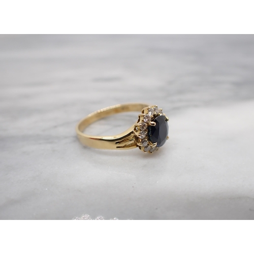 182 - A Sapphire and Diamond cluster Ring claw-set oval-cut sapphire within a frame of fourteen brilliant-... 