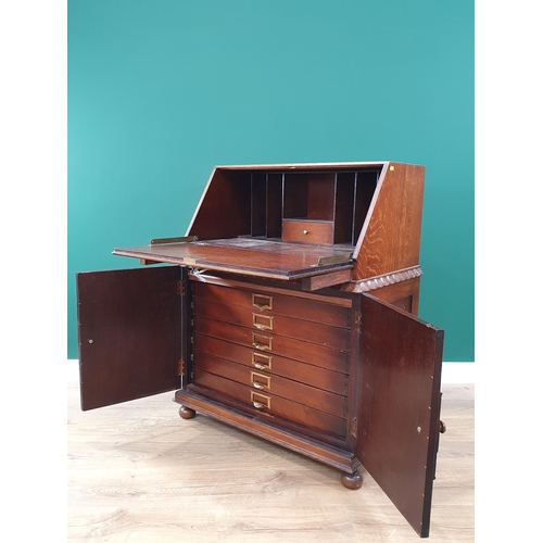 718 - A mid Century oak Bureau having a pair of cupboard doors enclosing drawers with brass engraved dedic... 