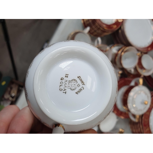 319 - A large quantity of 'Sunny' china dinnerware, decorated gilding and red borders, some chipped