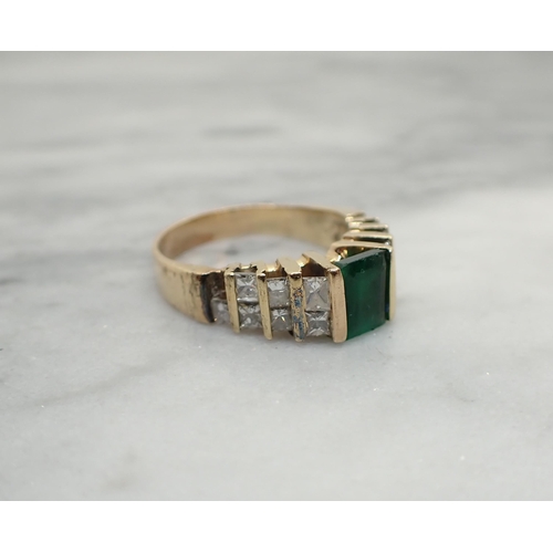 153 - An Emerald and Diamond Ring channel-set step-cut emerald between graduated pairs of princess-cut dia... 