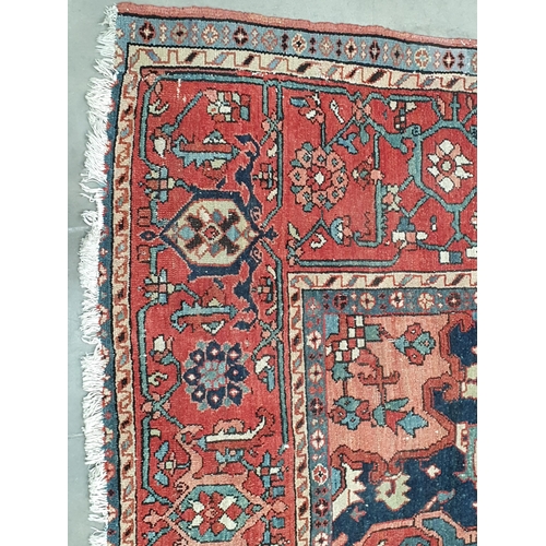 386 - A Heriz Rug with central all over geometric designs in blue, geometric pattern border, on a red grou... 