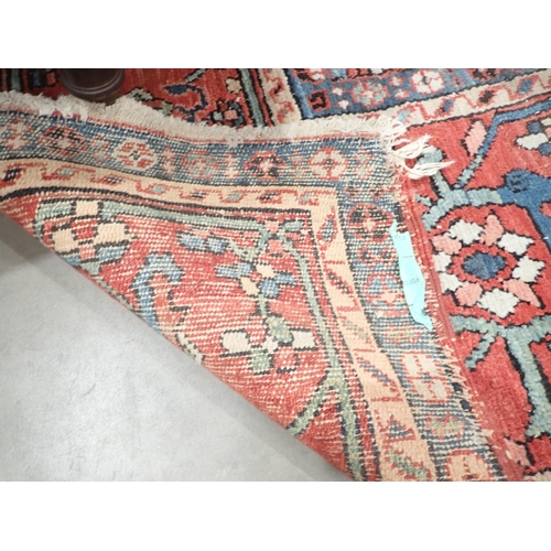 386 - A Heriz Rug with central all over geometric designs in blue, geometric pattern border, on a red grou... 