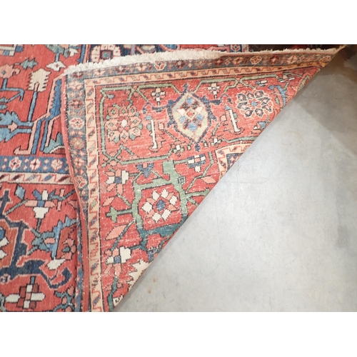 386 - A Heriz Rug with central all over geometric designs in blue, geometric pattern border, on a red grou... 