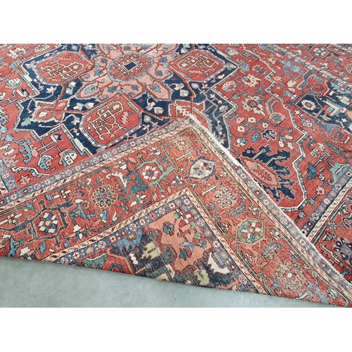 386 - A Heriz Rug with central all over geometric designs in blue, geometric pattern border, on a red grou... 