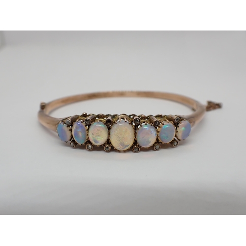 156 - An Opal and Diamond hinged Bangle the front claw-set seven graduated oval opal cabochons with rose-c... 