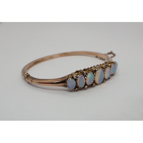 156 - An Opal and Diamond hinged Bangle the front claw-set seven graduated oval opal cabochons with rose-c... 