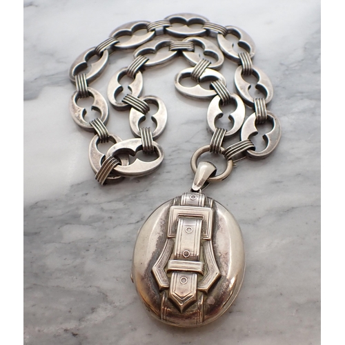 151 - An oval silver Locket with applied buckle to front on fancy link chain, unmarked