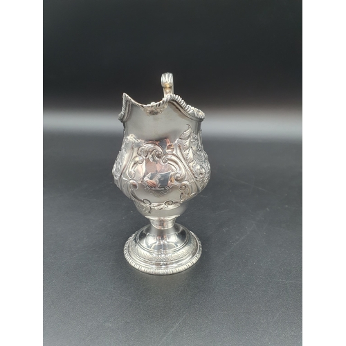 108 - A George III silver helmet shape cream Jug with floral embossing and engraved crest London 1772