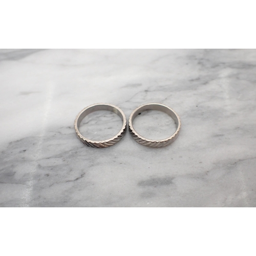 175 - A pair of white metal Wedding Bands with engraved finish, one marked 18ct, approx 6.60gms