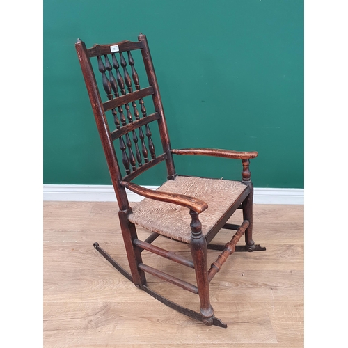 32 - An oak and elm rush seated Spindle back Rocking Chair, on metal rockers.