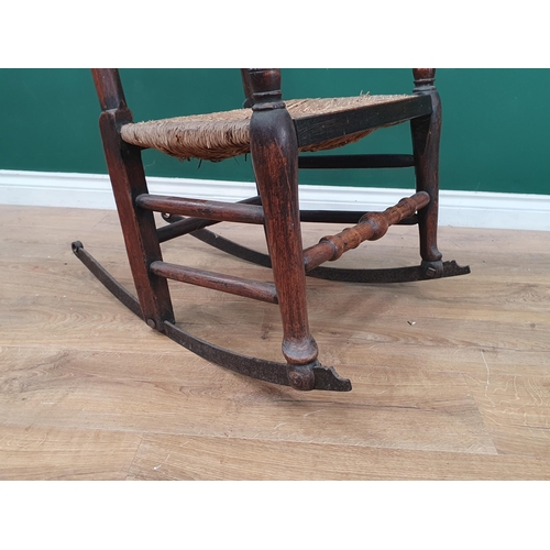 32 - An oak and elm rush seated Spindle back Rocking Chair, on metal rockers.