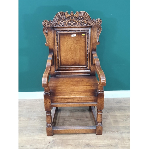 48 - An oak Wainscot Armchair in the 17th Century style with carved serpent cresting rail above plain pan... 