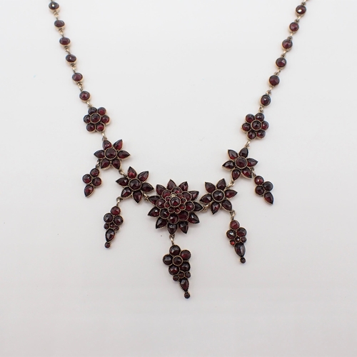 163 - A Garnet Fringe Necklace with graduated rosettes each suspending a drop set rose-cut stones througho... 