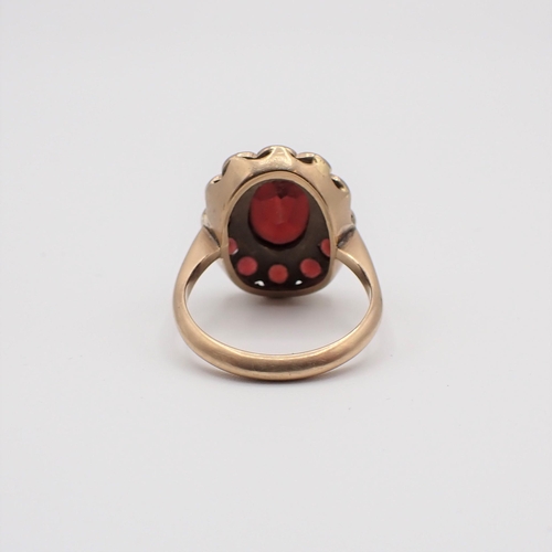 165 - A Garnet Cluster Ring rubover-set oval-cut stone within a frame of round stones in 9ct gold, ring si... 