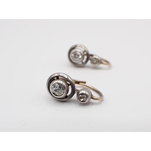 143 - A pair of Diamond Earrings each rubover-set old-cut stone below smaller stone in silver backed with ... 