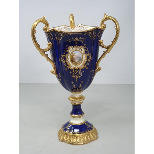 391 - A Coalport three handled Goblet with rich blue ground and reserves of landscapes framed within gilt ... 