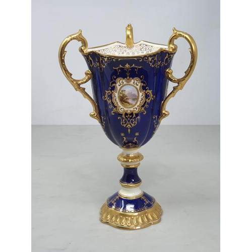 391 - A Coalport three handled Goblet with rich blue ground and reserves of landscapes framed within gilt ... 