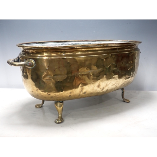 446 - A two handled brass Jardiniere, oval and with embossed coat of arms on four paw supports, 2ft W