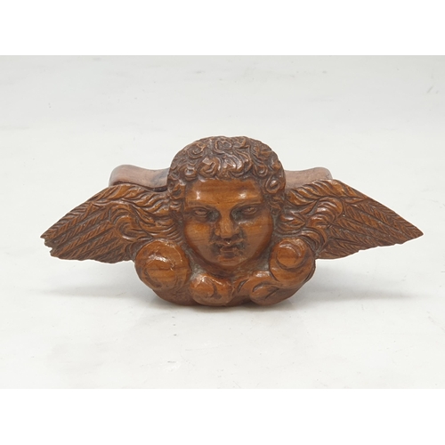 543 - A treen Snuff Box, the lid in the form of a winged Cherub, an olive wood Compact Mirror, a carved tr... 