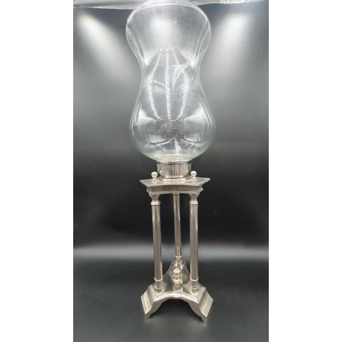 56 - A plated Candle Stand having triple column supports surmounted by clear glass bell shape shade, 2ft