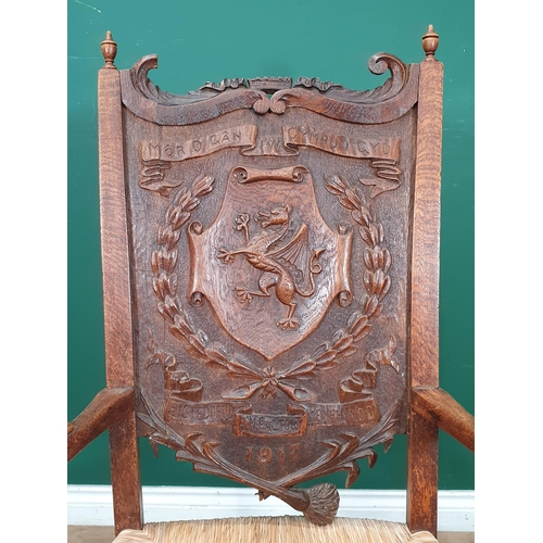 908 - A carved oak Eisteddfod Elbow Chair the back carved with dragon in a panel and dated 1917, with rush... 