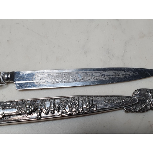 241 - An Australian white metal Knife with embossed Scenes of figures on handle and sheath and engraved sc... 