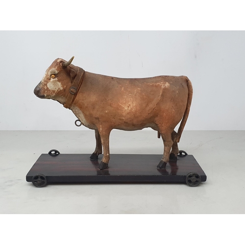 28 - An antique folk art leather covered pull-along Cow on rosewood effect stained base 7in H