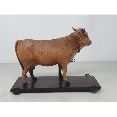 28 - An antique folk art leather covered pull-along Cow on rosewood effect stained base 7in H