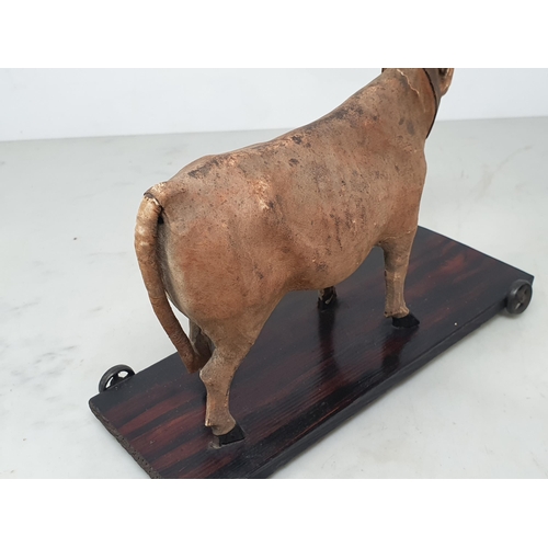 28 - An antique folk art leather covered pull-along Cow on rosewood effect stained base 7in H