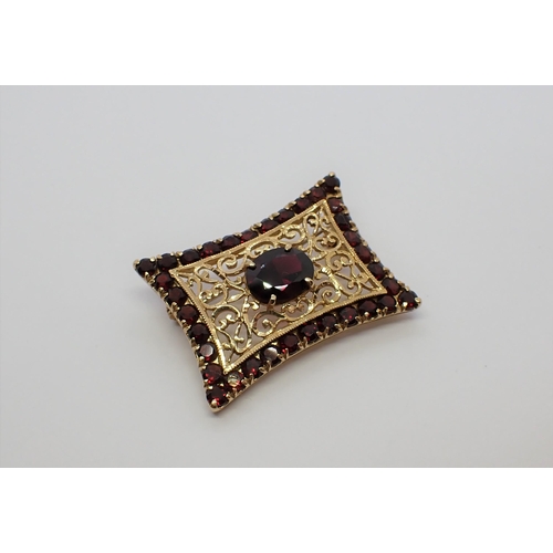 180 - A Garnet Brooch the scrolled openwork plaque claw-set oval-cut stone within outer frame of round sto... 