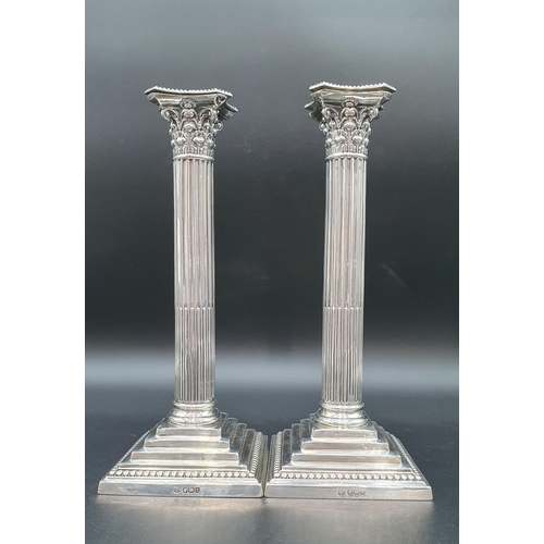 114 - A pair of George V silver Candlesticks with fluted columns, corinthian capitals on stepped beaded sq... 