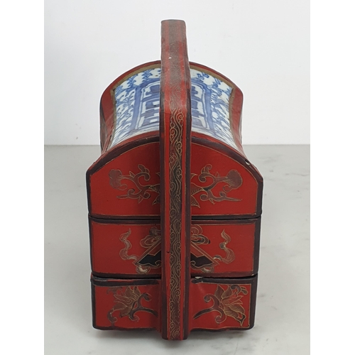 313 - A Chinese three tier lacquered Tiffin Carrier, the lid with inset blue and white tile, with red lacq... 