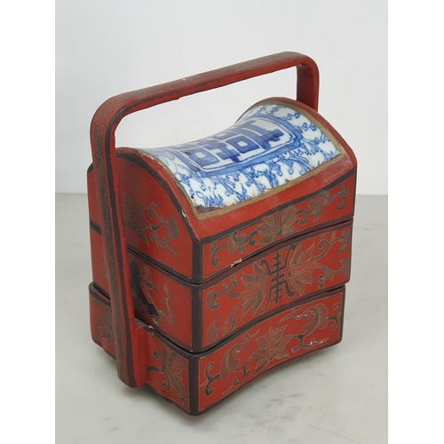 313 - A Chinese three tier lacquered Tiffin Carrier, the lid with inset blue and white tile, with red lacq... 