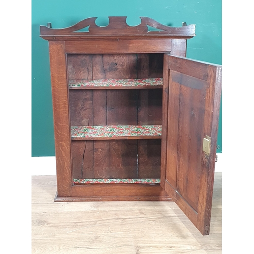 548 - An 18th Century oak hanging Cupboard with shaped surmount, fitted single panelled door enclosing she... 