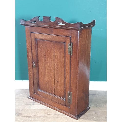 548 - An 18th Century oak hanging Cupboard with shaped surmount, fitted single panelled door enclosing she... 