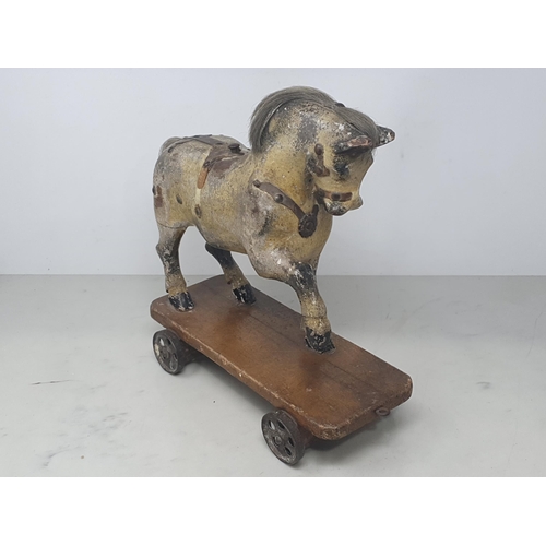 642 - An antique carved and dapple painted pull along Horse on stained wooden base with metal wheels 11in ... 