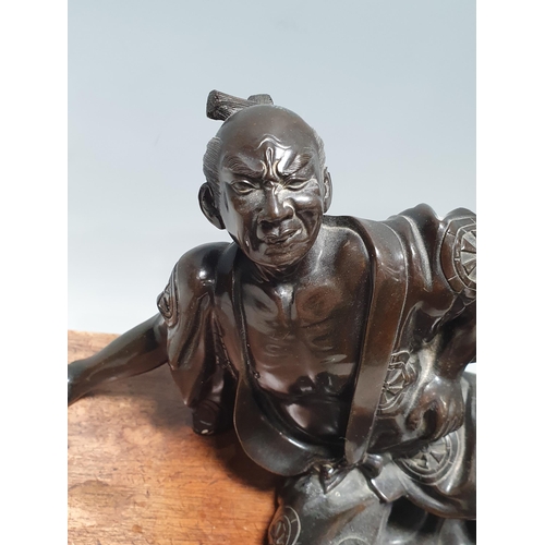 306 - A Chinese bronze Sculpture of a man in robes falling over, on associated hardwood Stand 6 1/2in H