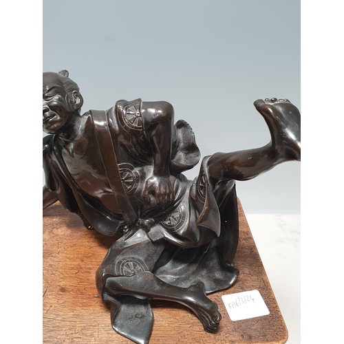 306 - A Chinese bronze Sculpture of a man in robes falling over, on associated hardwood Stand 6 1/2in H