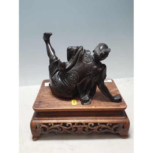 306 - A Chinese bronze Sculpture of a man in robes falling over, on associated hardwood Stand 6 1/2in H