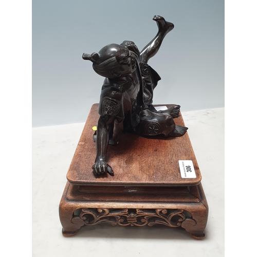 306 - A Chinese bronze Sculpture of a man in robes falling over, on associated hardwood Stand 6 1/2in H