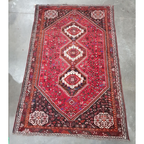 67 - A Persian Rug with three central lozenges surrounded by stylised motifs on a red ground, 8ft 5in x 5... 