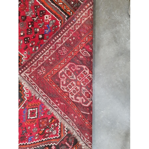 67 - A Persian Rug with three central lozenges surrounded by stylised motifs on a red ground, 8ft 5in x 5... 