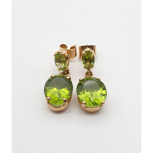 169 - A pair of Peridot drop Earrings each claw-set oval-cut stone suspending larger mixed-cut stone