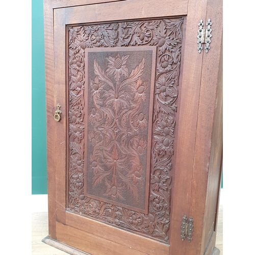 11 - An Arts & Crafts walnut Cupboard with carved floral decorated panelled door enclosing fitted shelves... 