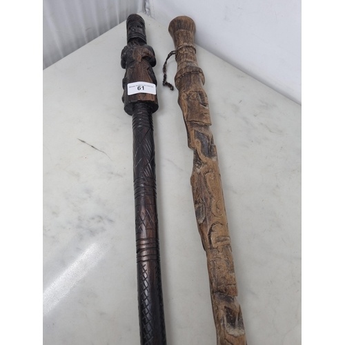 61 - Two African Tribal Walking Sticks carved figures, one holding an object, approx 3ft (R3)