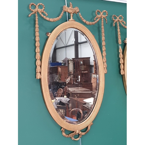 408 - A pair of Regency style gilt framed oval Wall Mirrors with urn surmounts and swag and ribbon decorat... 