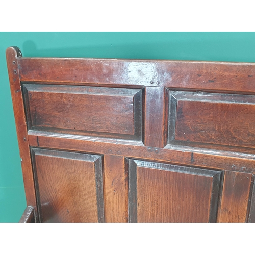 445 - An 18th Century oak Settle with multiple fielded panels to the back, shaped arms on squared supports... 